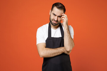 Young puzzled troubled pensive man 20s barista bartender barman employee in black apron white t-shirt work in coffee prop up forehead head isolated on orange background studio Small business startup.