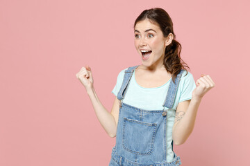 Young fun overjoyed excited happy caucasian woman in trendy denim clothes blue tshirt do winner gesture clench fist scream isolated on pastel pink background studio portrait. People lifestyle concept