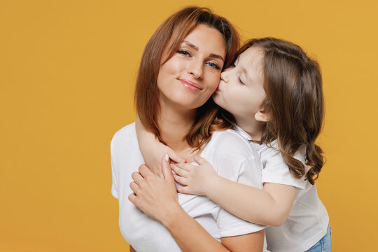 Happy woman in basic white t-shirt have fun with cute child baby girl 5-6 years old hugs. Mommy little kid daughter isolated on yellow orange color background studio. Mother's Day love family concept.