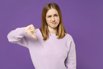 Fototapeta premium Young serious strict disappointed student woman 20s wearing purple knitted sweater show thumb down dislike gesture refusing say no isolated on violet color background studio People lifestyle concept