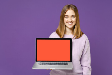 Young smiling positive happy freelancer student caucasian woman 20s in purple knitted sweater using laptop pc computer with blank screen workspace area isolated on violet background studio portrait