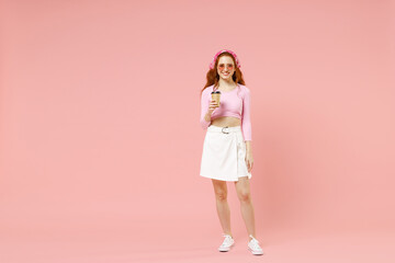 Full length young smiling happy caucasian woman wearing rose clothes bandana glasses hold paper cup of coffee drink hot tea isolated on pastel pink color background studio People lifestyle concept