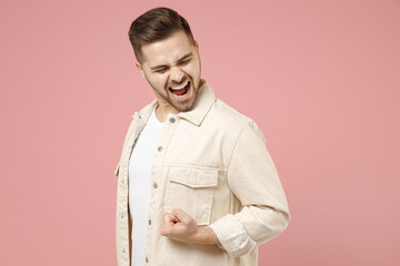 Young overjoyed happy positive trendy excited caucasian man in jacket white t-shirt do winner gesture clench fist celebrate isolated on pastel pink background studio portrait People lifestyle concept