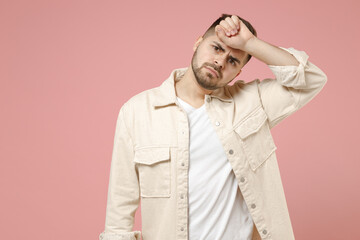Young troubled sick ill pensive thoughtful sad man 20s in jacket white t-shirt put hand on forehead have headache migraine isolated on pastel pink background studio portrait People lifestyle concept