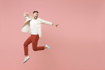 Fototapeta na wymiar Full length young smiling excited overjoyed joyful fashionable caucasian man 20s in jacket white t-shirt jump high point index finger aside on workspace area isolated on pastel pink background studio.