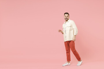 Fototapeta premium Full length young smiling happy confident joyful fun trendy fashionable friendly caucasian man 20s wearing jacket white t-shirt walking going strolling isolated on pastel pink color background studio.