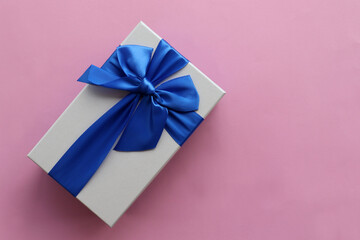 Gift box with blue ribbon on pink paper background. Mothers day present for mom or birthday gift. Top view, copy space