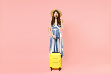 Full length traveler tourist woman in summer clothes, hat hold yellow suitcase spread hand isolated on pastel pink background Passenger traveling abroad on weekends getaway Air flight journey concept