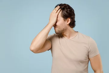 Foto op Canvas Young confused mistaken ashamed caucasian man 20s wearing casual basic beige t-shirt put hand on face facepalm epic fail gesture isolated on pastel blue background studio portrait. LIfestyle concept. © ViDi Studio