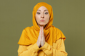 Young pleaded arabian asian muslim woman in abaya hijab yellow clothes hands folded in prayer...