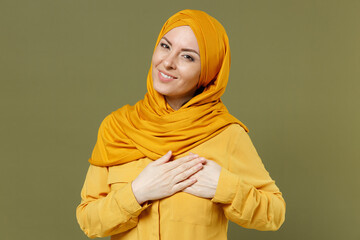 Kind-hearted smiling young arabian asian muslim woman 20s in abaya hijab yellow clothes put folded...