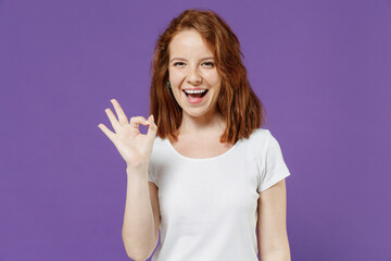 Obraz na płótnie Canvas Young fun smiling happy friendly caucasian woman 20s wearing white basic blank print design t-shirt show ok okay gesture isolated on dark violet background studio portrait. People lifestyle concept