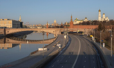 Obraz premium Early morning on the Moscow river. View of the Moscow Kremlin and the stone bridge. Reflection in water. Empty road along the embankment and a temple in the background