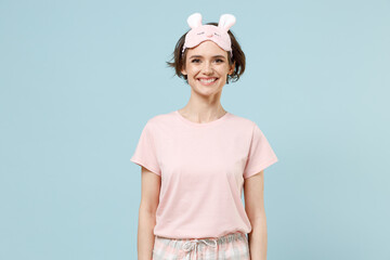 Calm young smiling caucasian woman 20s wearing pajamas jam sleep eye mask rest relaxing at home look camera isolated on pastel blue color background studio portrait. Good mood night bedtime concept.