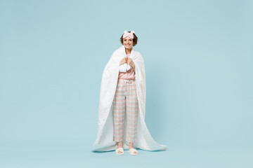 Fototapeta na wymiar Full length young smiling woman in pajamas jam sleep eye mask rest relax at home wrap covered under blanket duvet look camera isolated on pastel blue background studio Good mood night bedtime concept.