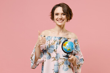 Young happy smiling geography student teacher caucasian woman with short hairdo in blouse hold in hands Earth world globe show thumb up like gesture isolated on pastel pink color background studio