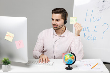 Employee operator business man in set microphone headset helpline assistance sit work at call center office desk computer card sign HELP title text browse internet search isolated on grey background