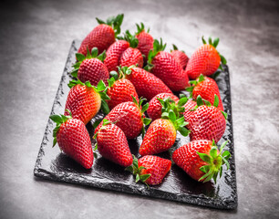Strawberries fresh ready to eat vibrant color arrangement on black shiny stone cutting board and marble kitchen table front view studio shot

