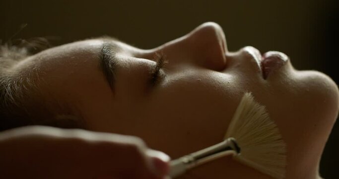 Close up of relaxing thai massage with cosmetic brushes. Face of woman enjoying cleansing body care brush massage in wellness resort spa 4k footage