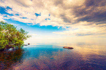 The boundless lake surface in calm weather. View from the shore. Stones in the water. Cumulus clouds. Summer day. Beautiful nature. Russia, Europe.
