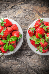 Strawberries fresh overhead ready to eat spring arrangement with green leaves in white ceramic jars on wooden table in studio
