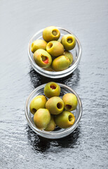Green fresh olives stuffed with peppers front view ready to eat arrangement in glass jars on shiny stone kitchen restaurant table close up studio shot