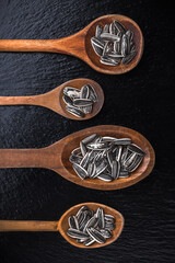 Sunflower seeds large overhead close-up arrangement in old wooden spoons on black shiny stone kitchen restaurant table studio shot

