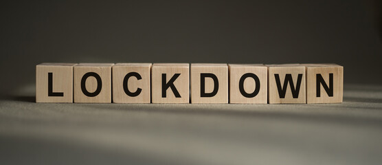 A wooden blocks with the word LOCKDOWN written on it on a gray background.