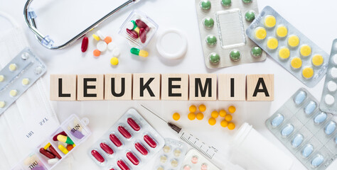 LEUKEMIA word on wooden blocks on a desk. Medical concept with pills, vitamins, stethoscope and syringe on the background.