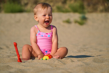 Happy baby in the sand plays. Cheerful little kid playing on the beach on a sunny day. High quality photo