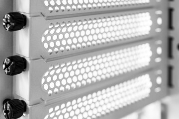 Horizontal ventilation grille. Mounting screws. Air vents. Metal construction. Angle view. Black and white tones.