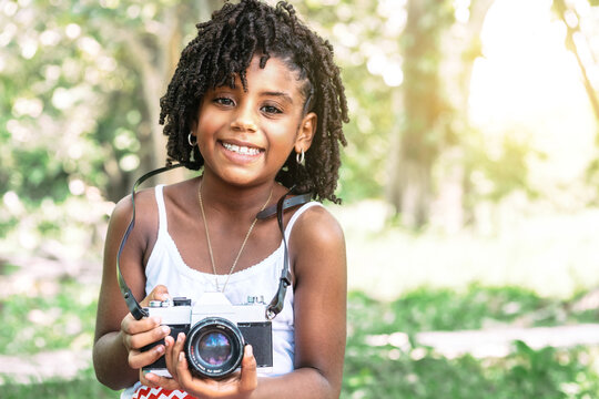 young african american toddler girl holding an old camera and looking at camera.
