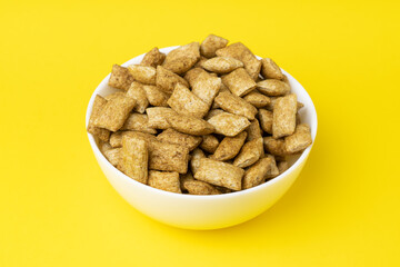 Rye and oats breakfast pads with cinnamon in white ceramical bowl on vivid yellow background.