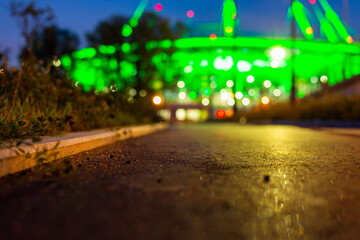 Illumination on the building. Pedestrian sidewalk. Alley with trees and lanterns. Grass growing on the lawn. Close up view from curb stone level.