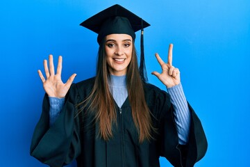 Beautiful brunette young woman wearing graduation cap and ceremony robe showing and pointing up with fingers number eight while smiling confident and happy.
