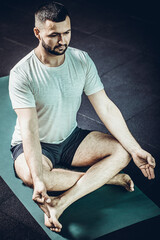 Man yoga practice pose. Young men do yoga indoors on black mat. Guy exercising yoga with a black background in gym. Young men meditating in lotus posture closeup. Training concept.