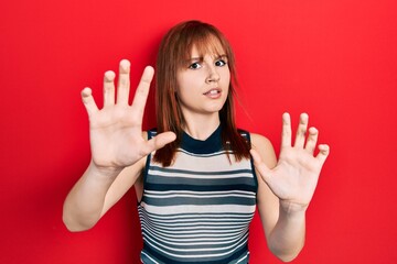 Redhead young woman wearing casual t shirt afraid and terrified with fear expression stop gesture with hands, shouting in shock. panic concept.