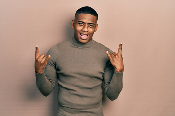 Fototapeta premium Young black man wearing casual turtleneck sweater shouting with crazy expression doing rock symbol with hands up. music star. heavy concept.