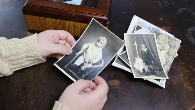 female hands fingering memorabilia in an old wooden box, a stack of retro photos, a lock of hair, vintage photographs of 50s, 60s, concept of family tree, genealogy, childhood memories