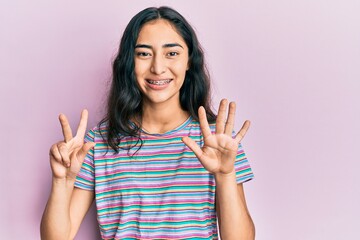 Hispanic teenager girl with dental braces wearing casual clothes showing and pointing up with fingers number eight while smiling confident and happy.