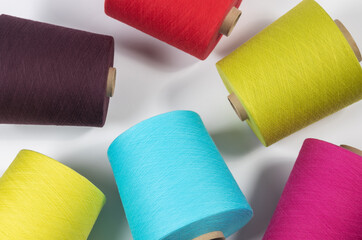 Large spools of brightly colored thread lie in a chaotic pattern on a white backing. View from above