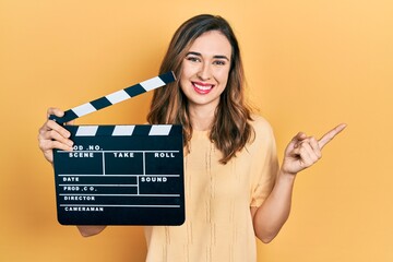 Young hispanic girl holding video film clapboard smiling happy pointing with hand and finger to the...