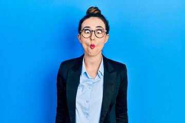 Young hispanic girl wearing business clothes and glasses making fish face with lips, crazy and comical gesture. funny expression.