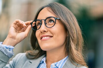 Young hispanic businesswoman smiling happy touching her glasses at the city.