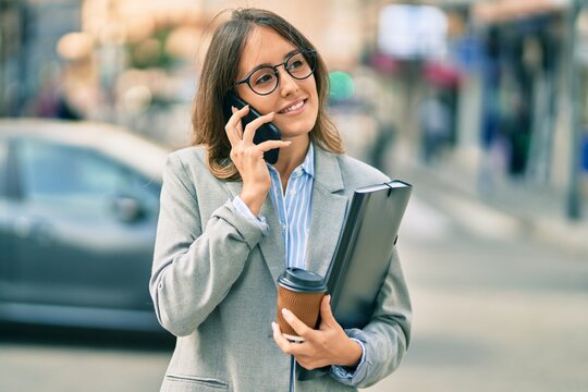 Young hispanic businesswoman talking on the smartphone and drinking take away coffee at the city.