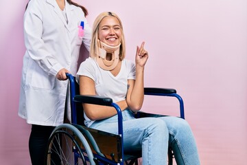 Fototapeta na wymiar Beautiful blonde woman sitting on wheelchair with collar neck with a big smile on face, pointing with hand and finger to the side looking at the camera.