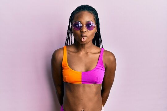 Young african american woman wearing bikini and sunglasses making fish face with lips, crazy and comical gesture. funny expression.