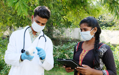 An Indian doctor holds an infrared thermometer and shares temperature readings with his assistant