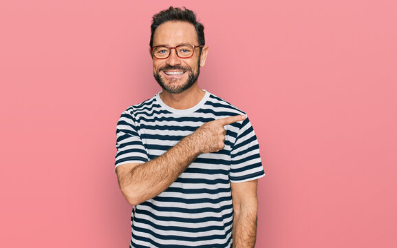 Middle age man wearing casual clothes and glasses cheerful with a smile of face pointing with hand and finger up to the side with happy and natural expression on face