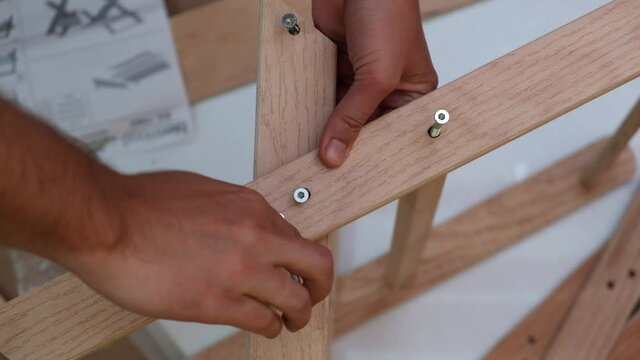 Close-up of man's hands assembling wooden children's chair with nails and allen wrench